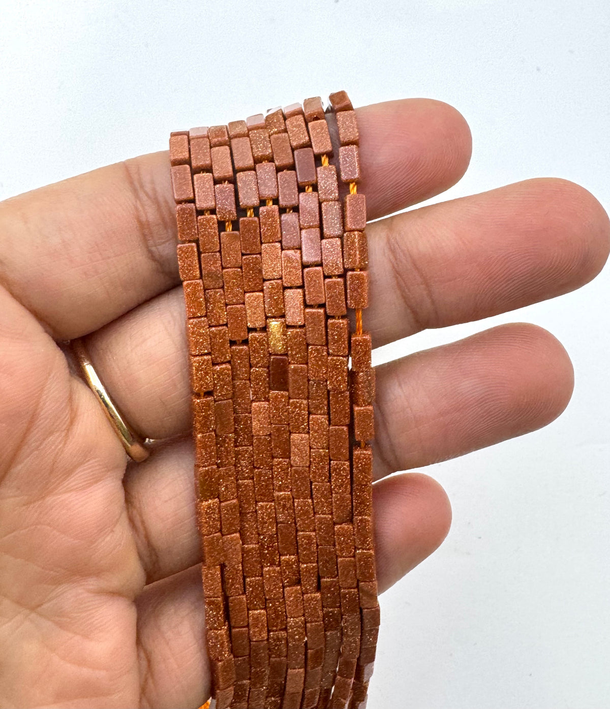 Gold Sandstone tube beads held in a person's hand against a plain white background.