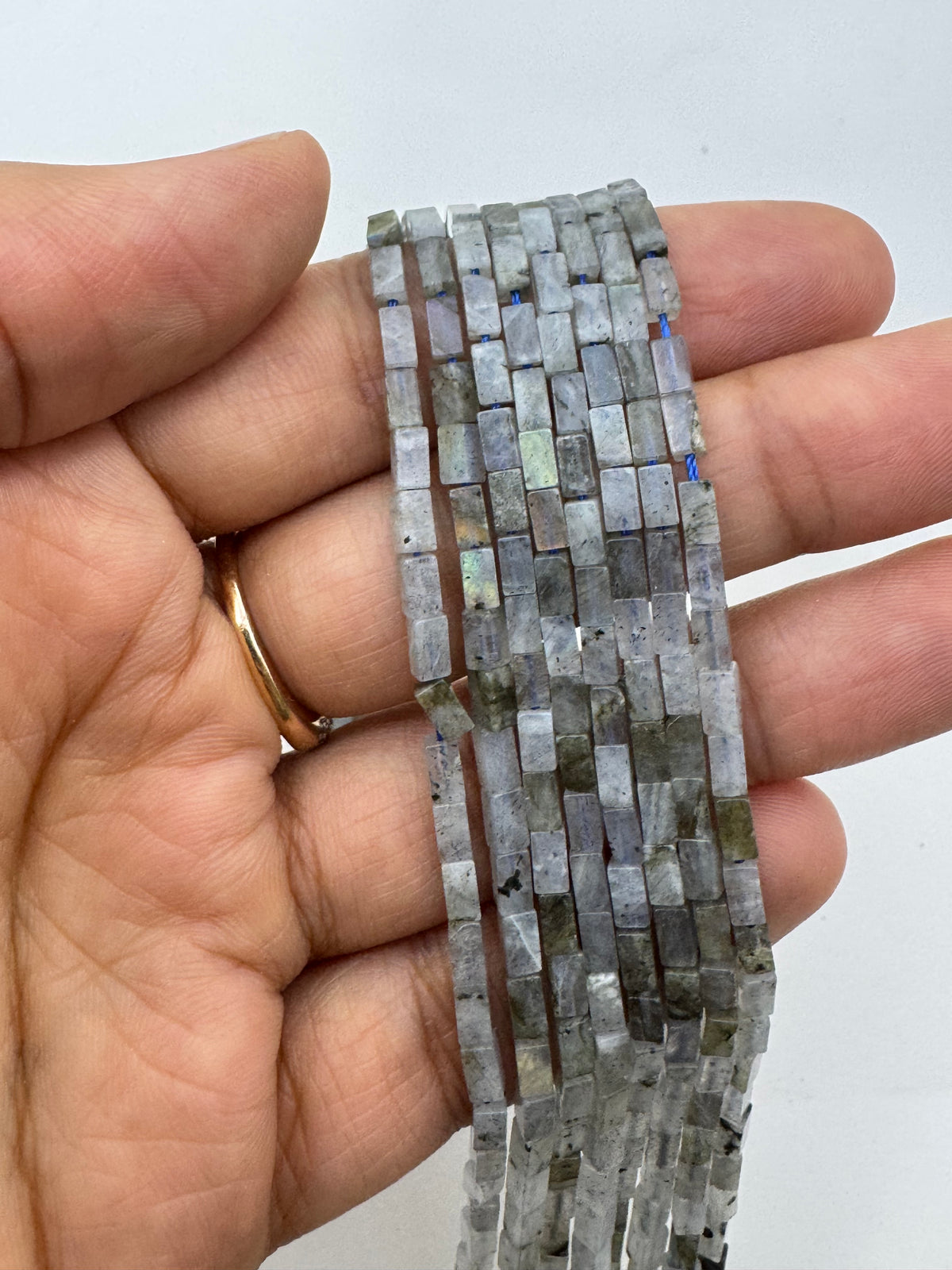 A hand holding a long strand of small rectangular labradorite beads that shimmer with gray, blue, and green iridescent colors.