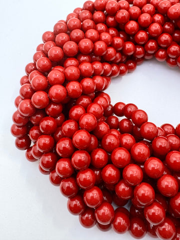 Multiple strands of glossy, polished red round shell pearl beads arranged in a spiral on a plain white background.
