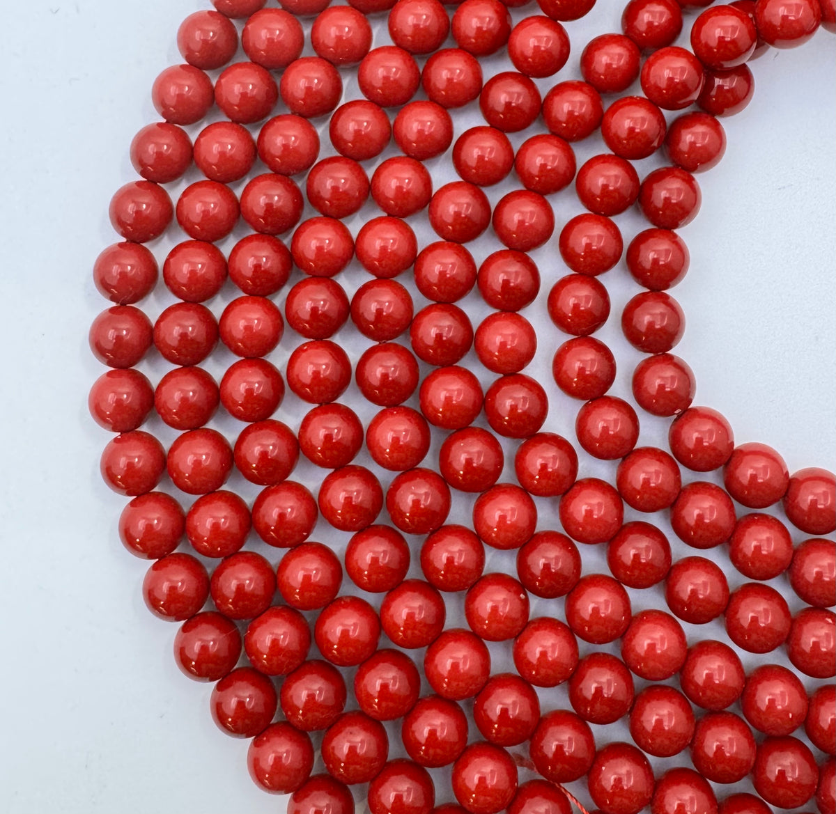 A close-up of glossy red shell pearl round beads arranged in curved strands on a plain light background.