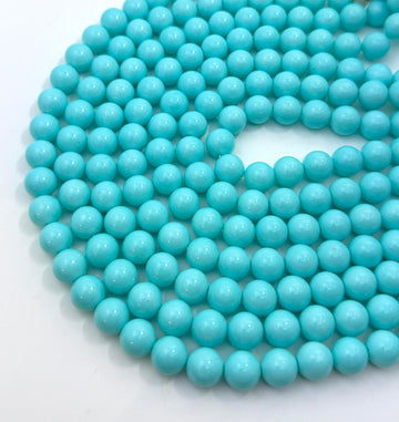 A close-up of a coiled strand of glossy, smooth turquoise-blue shell pearl beads on a plain white background.