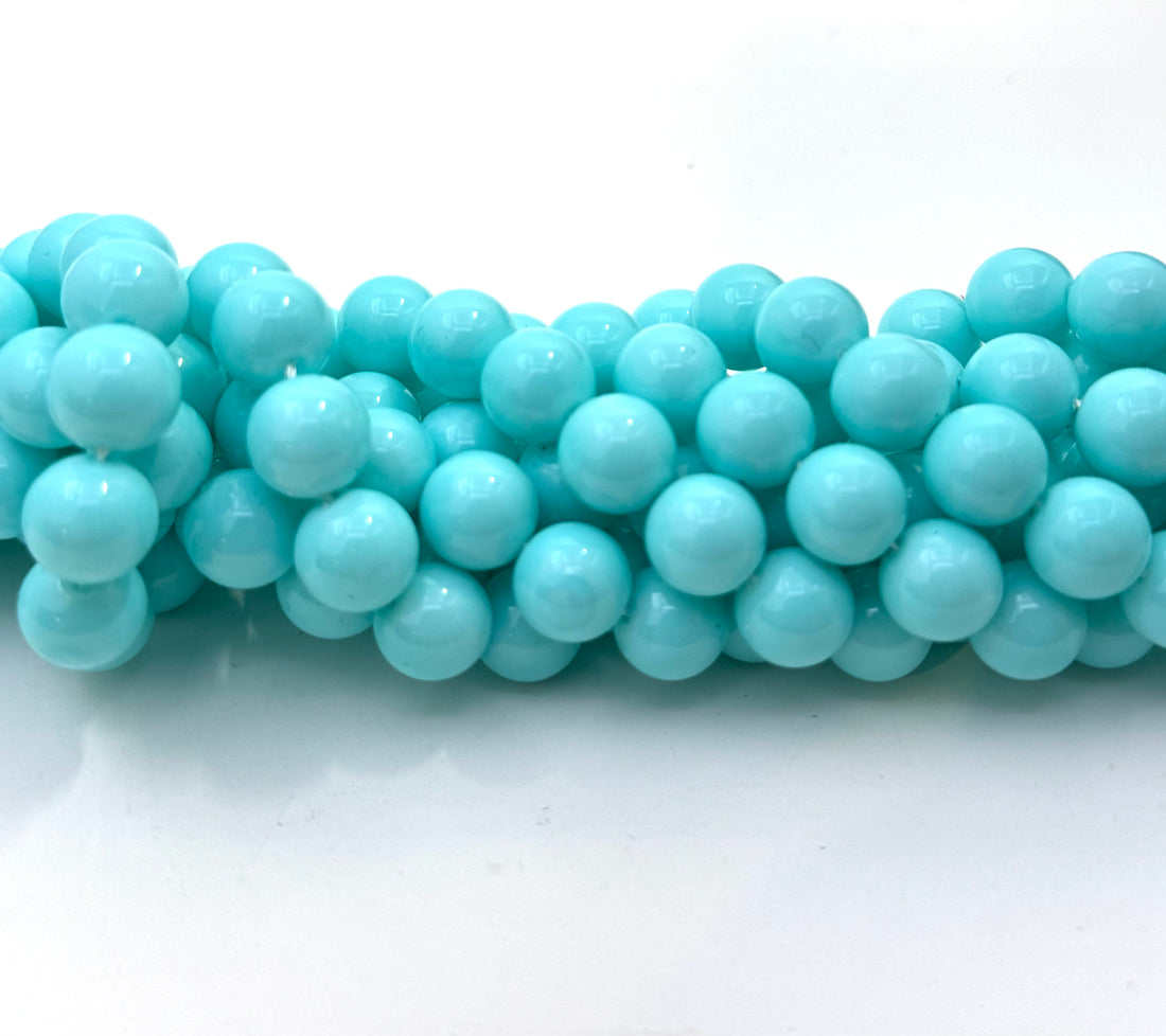 A close-up of a coiled strand of glossy, smooth turquoise-blue shell pearl beads on a plain white background.