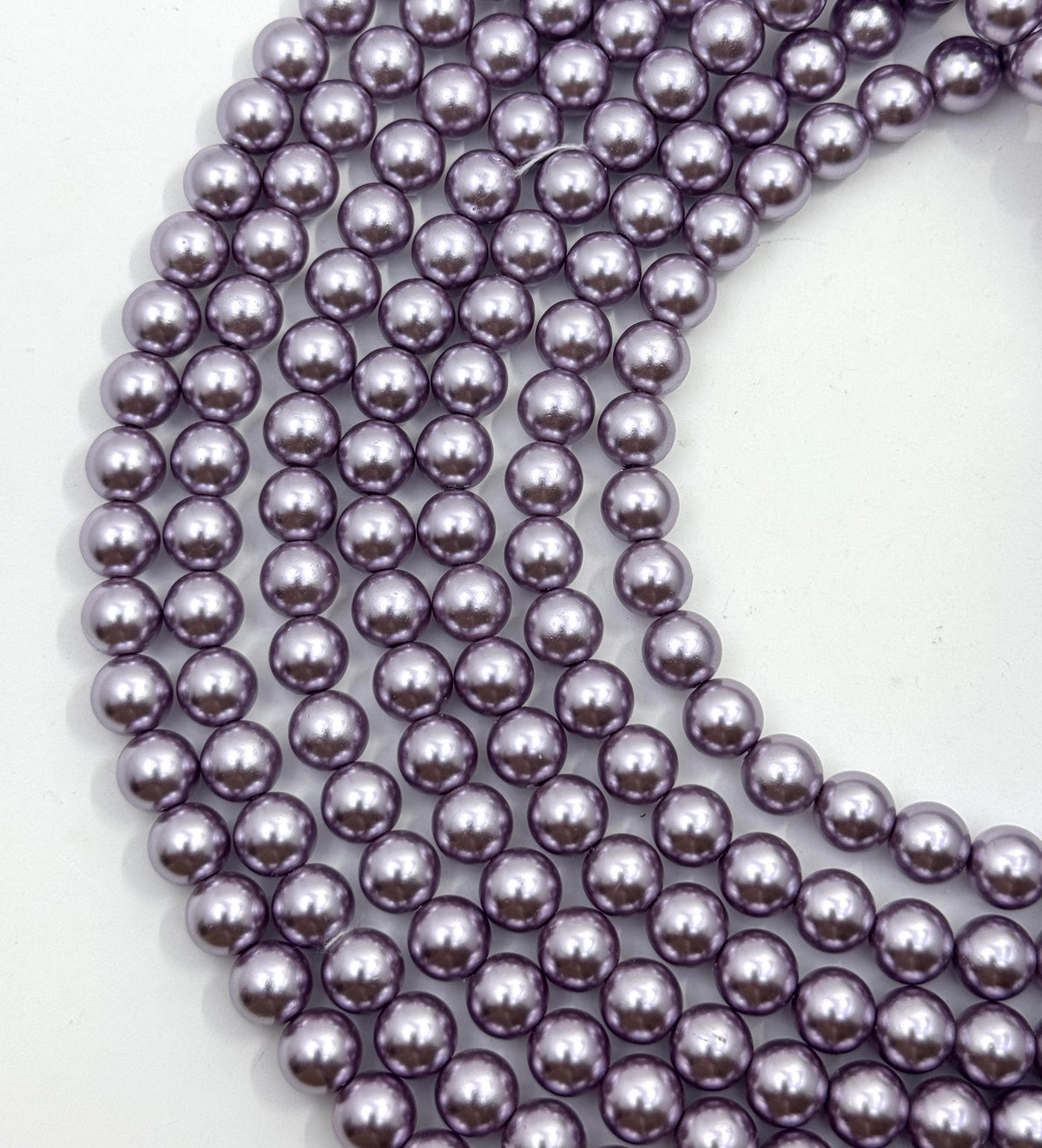 Multiple strands of glossy, lavender-purple shell pearl beads arranged in a curved pattern on a plain white background.