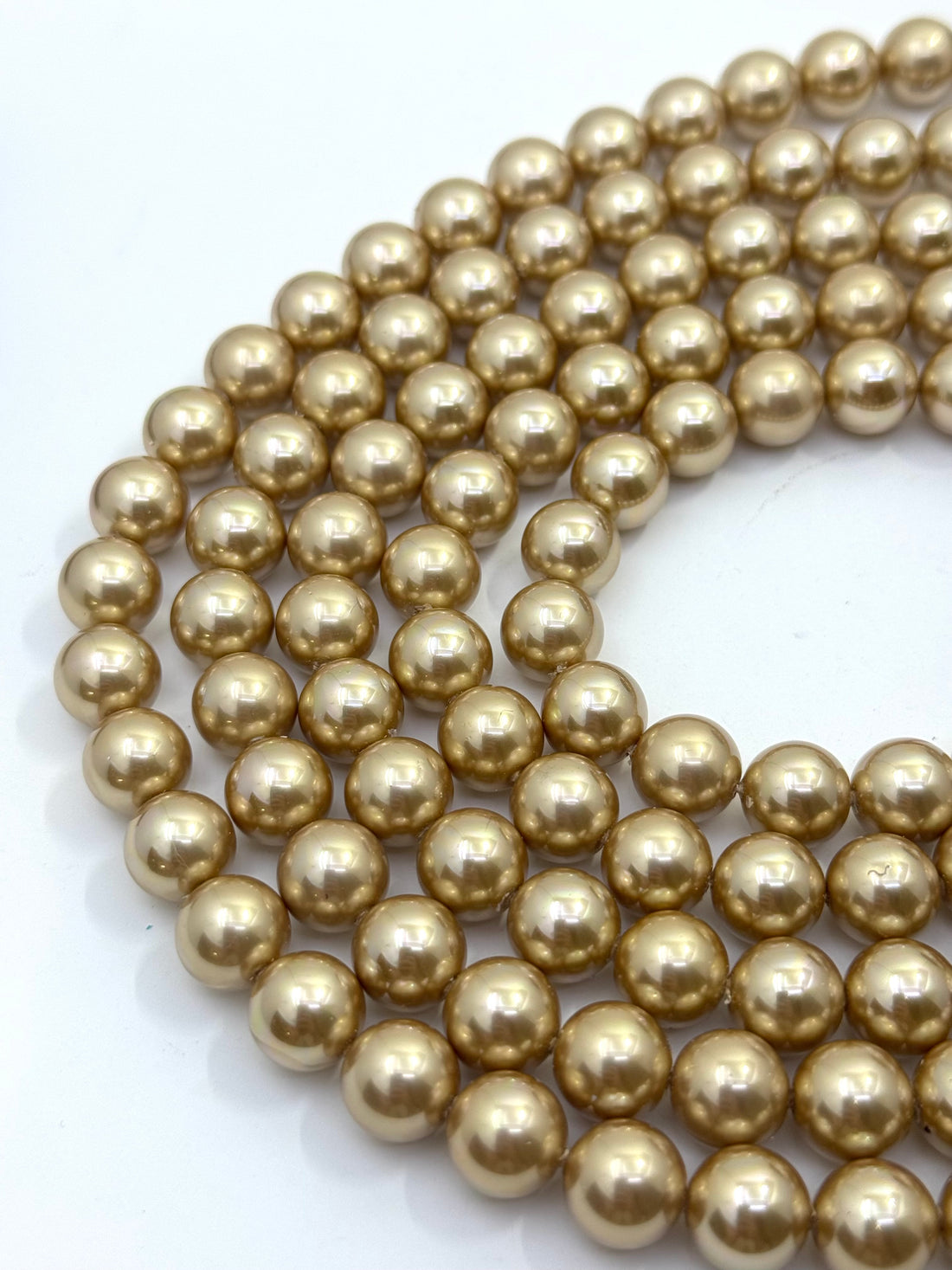 A hand holding a dense bundle of shiny metallic gold shell pearl round beads against a plain light background.