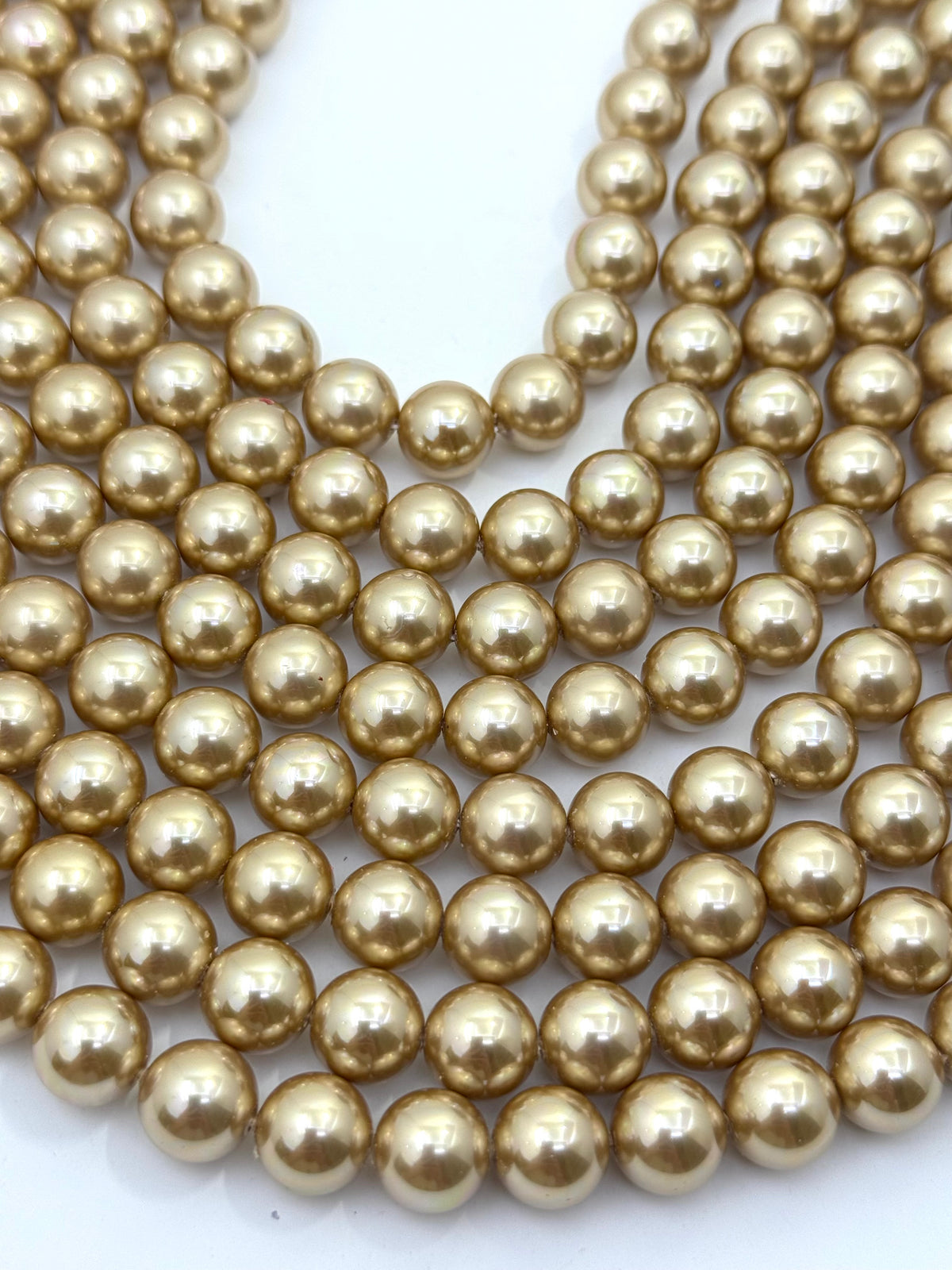 Multiple strands of shiny metallic gold shell pearl round beads arranged on a plain white background.