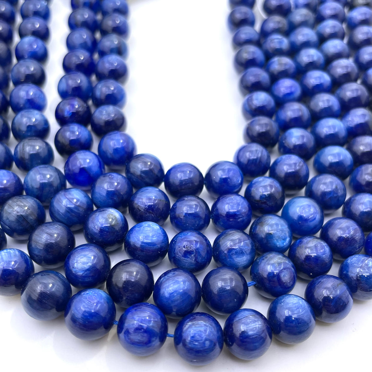 Multiple strands of polished round blue kyanite gemstone beads arranged on a white background.