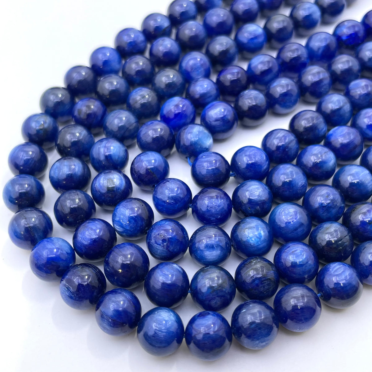 A close-up of round kyannite beads, arranged in overlapping strands on a white background.