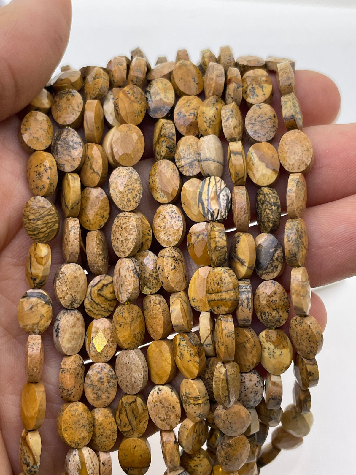 Flat oval faceted picture jasper on a hand for size reference
