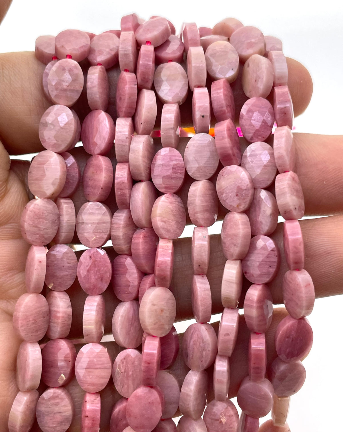 Flat oval faceted rhodonite on a hand for size reference