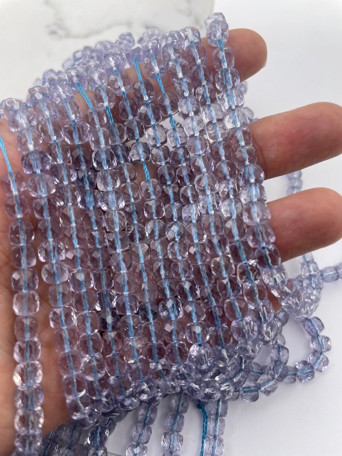 Blue cube faceted topaz beads on a hand for size reference