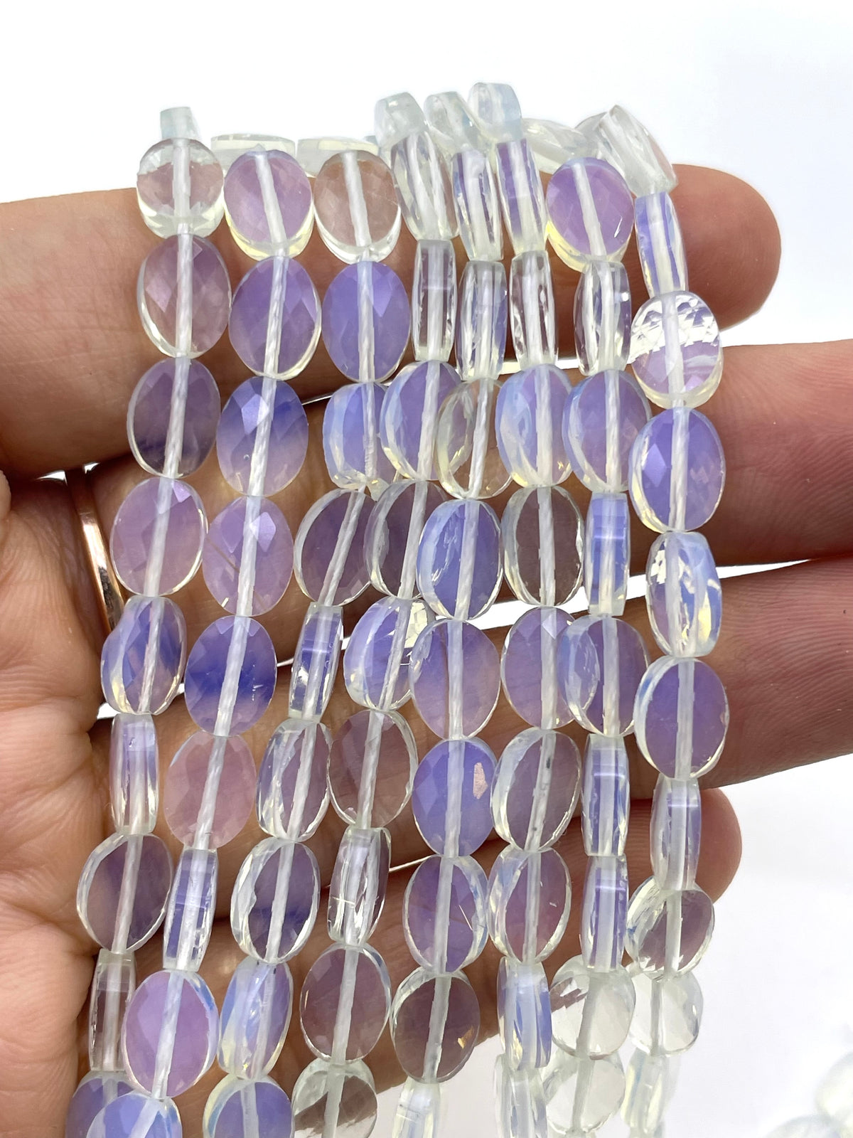 Flat oval faceted opalite on a hand for size reference
