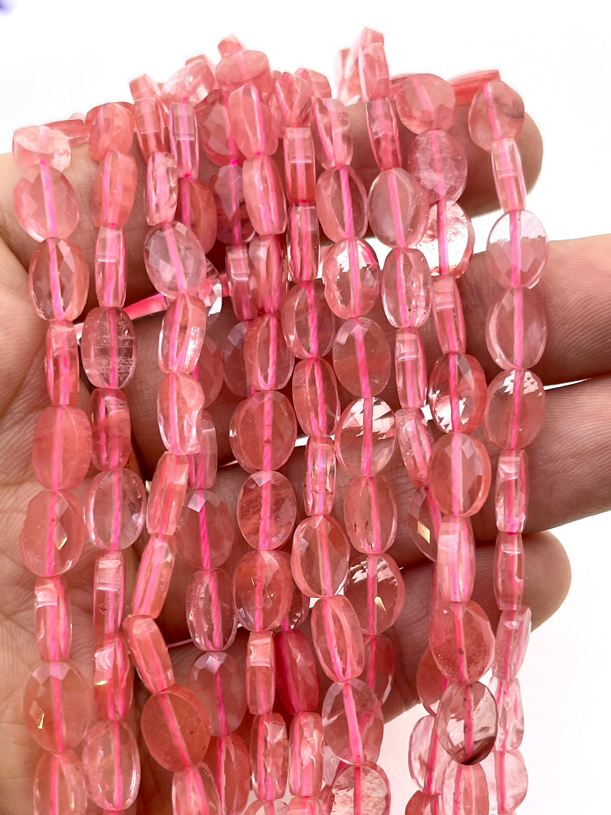 Flat oval faceted cherry quartz on a hand for size reference