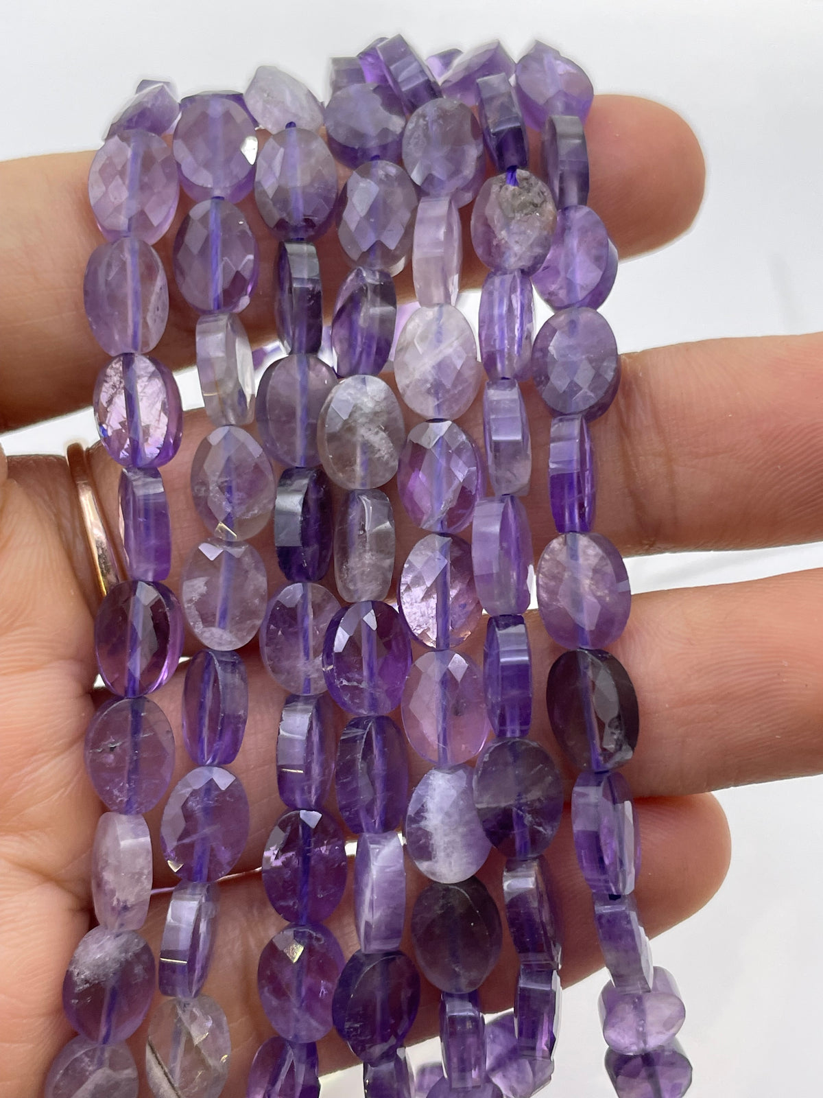 Flat oval faceted light amethyst on a hand for size reference