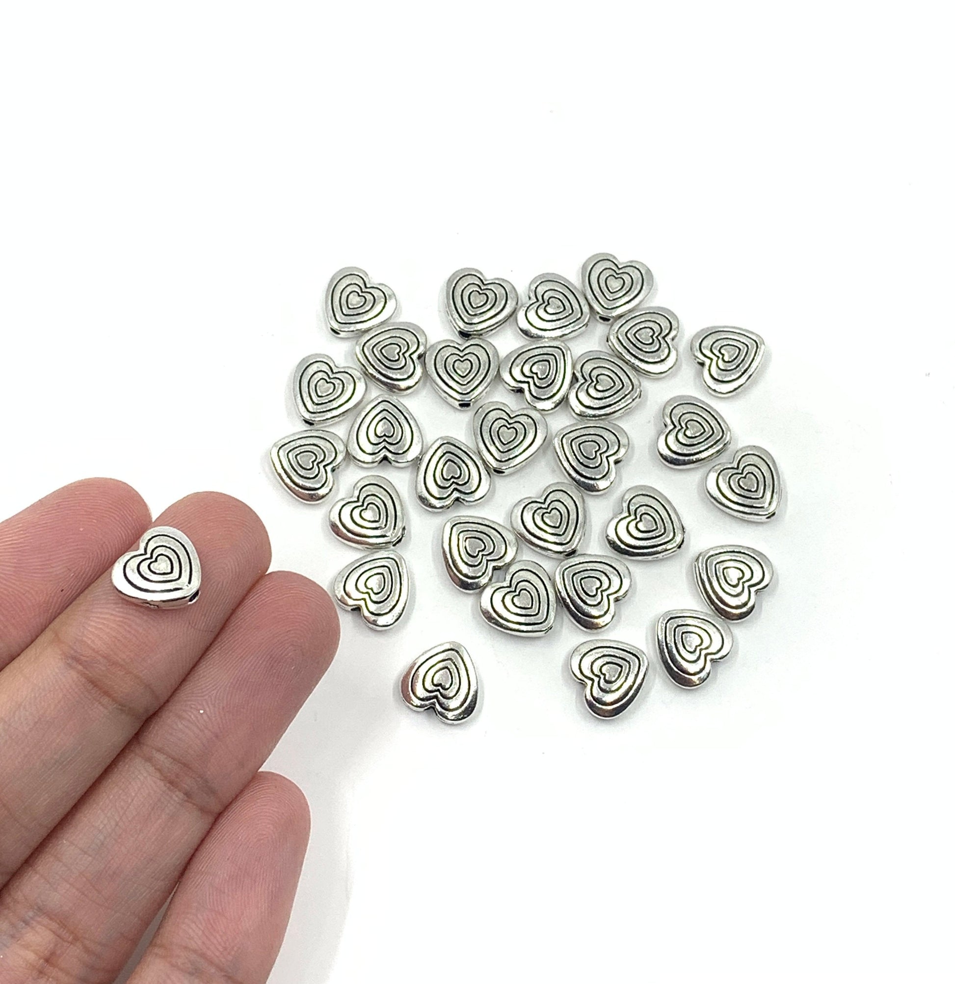 Heart beads shown on hand for size reference.